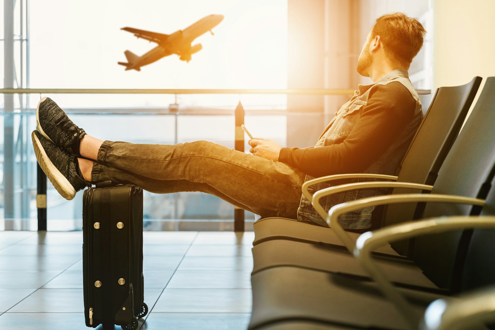 man sitting on gang chair with feet on luggage looking at airplane Mexico travel
